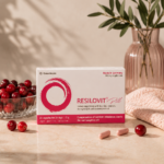 Συσκευασία του Resilovit® Pill σε απαλό ροζ σκηνικό, πλαισιωμένη από cranberries και κάψουλες, αναδεικνύοντας τη σύνθεσή του με βιταμίνες, μέταλλα, συνένζυμο Q10 και εκχύλισμα cranberry.
