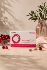 Συσκευασία του Resilovit® Pill σε απαλό ροζ σκηνικό, πλαισιωμένη από cranberries και κάψουλες, αναδεικνύοντας τη σύνθεσή του με βιταμίνες, μέταλλα, συνένζυμο Q10 και εκχύλισμα cranberry.