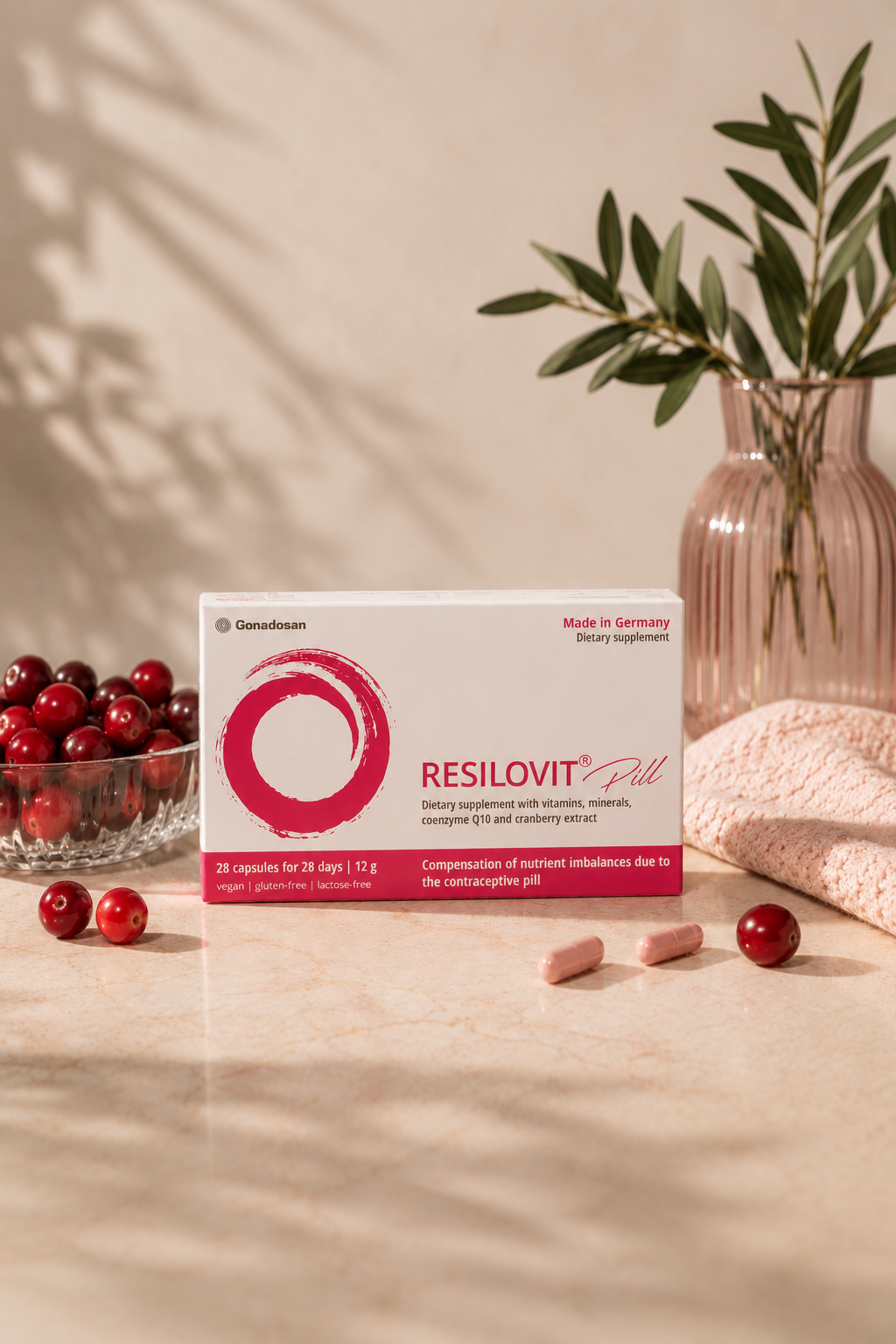 Resilovit® Pill - Συμπλήρωμα διατροφής για την κάλυψη των διατροφικών αναγκών κατά τη λήψη αντισυλληπτικών - Resilovit® Συσκευασία του Resilovit® Pill σε απαλό ροζ σκηνικό, πλαισιωμένη από cranberries και κάψουλες, αναδεικνύοντας τη σύνθεσή του με βιταμίνες, μέταλλα, συνένζυμο Q10 και εκχύλισμα cranberry.