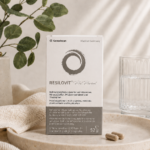 Συσκευασία του Resilovit® Pre Period σε minimal σκηνικό με φυσικές αποχρώσεις, δίπλα σε ποτήρι νερού, φυλλώματα και κάψουλες, αναδεικνύοντας τη σύνθεσή του με βιταμίνες, μέταλλα, φυτικά εκχυλίσματα και τρυπτοφάνη.