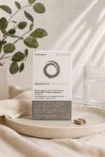 Συσκευασία του Resilovit® Pre Period σε minimal σκηνικό με φυσικές αποχρώσεις, δίπλα σε ποτήρι νερού, φυλλώματα και κάψουλες, αναδεικνύοντας τη σύνθεσή του με βιταμίνες, μέταλλα, φυτικά εκχυλίσματα και τρυπτοφάνη.