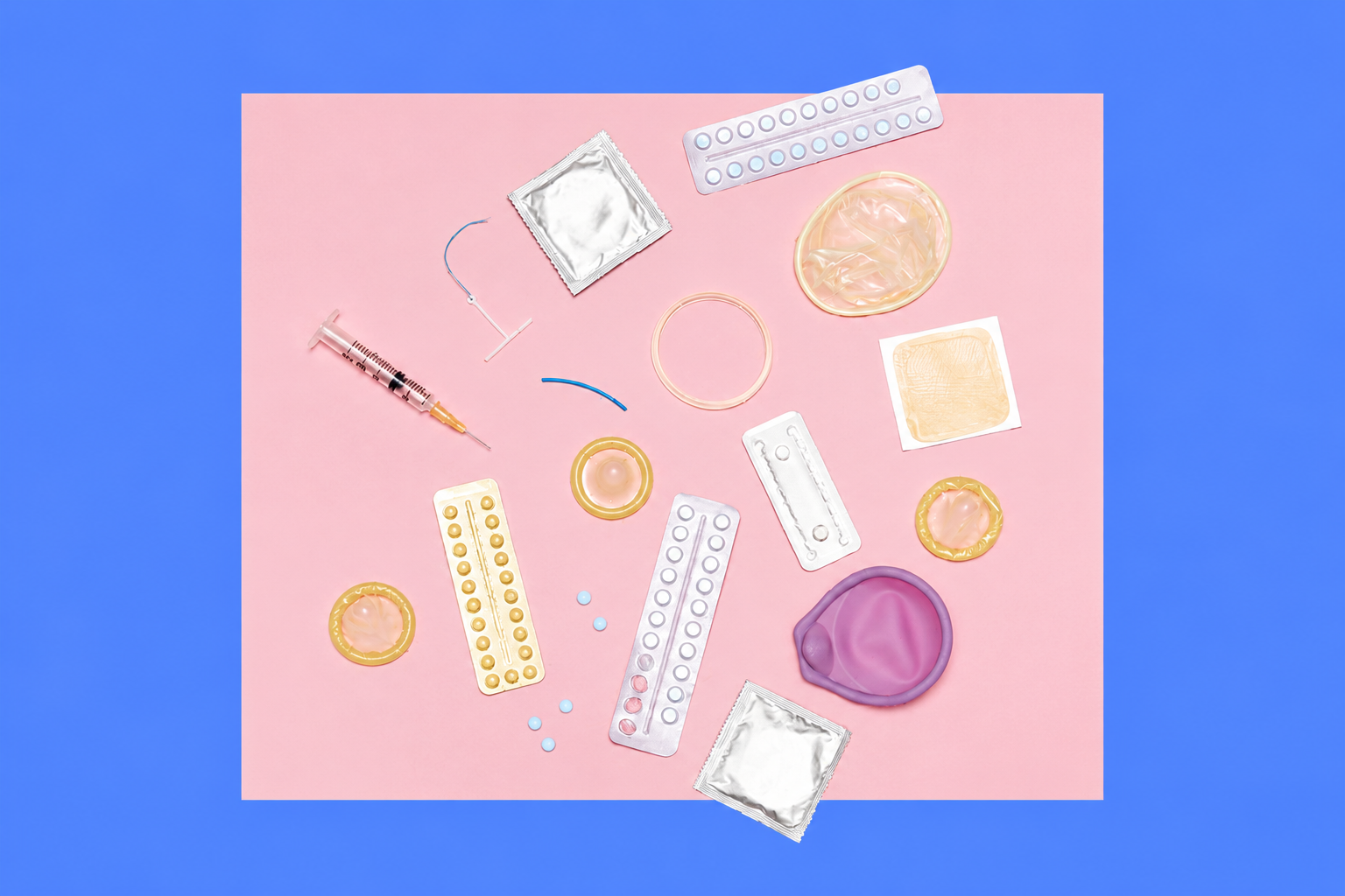 Assorted sexual health items scattered on a pink surface, including condoms, pill blister packs, a syringe, lubricant rings, and a purple sex toy with a blue backdrop.