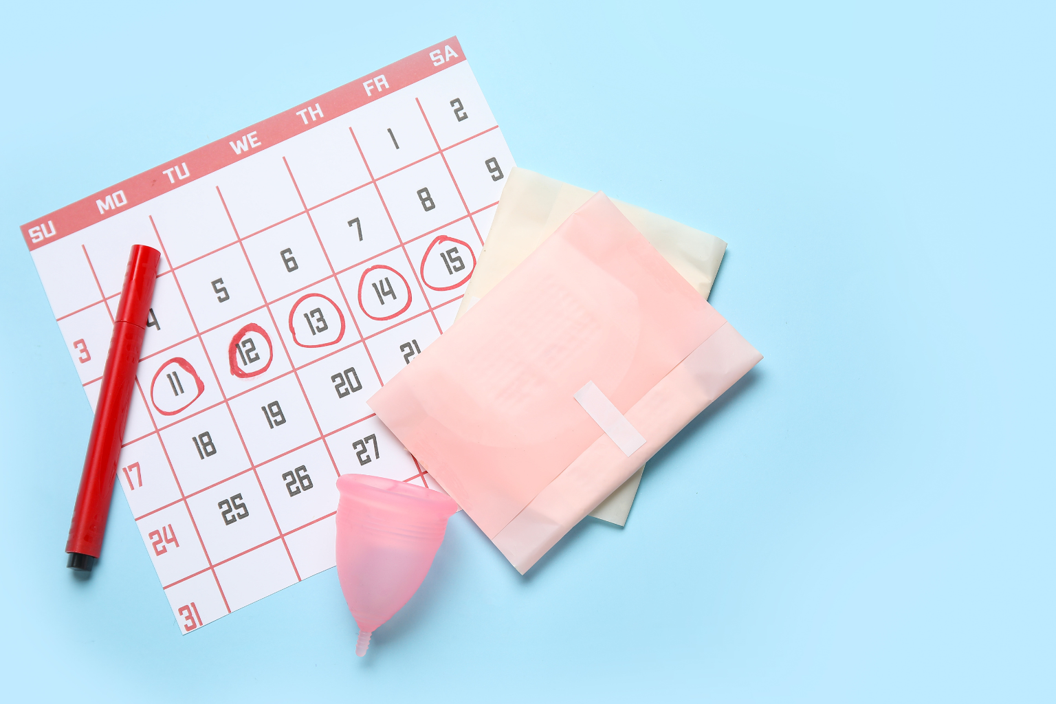 Calendar page with several dates circled in red, a red marker, and pink menstrual products on a light blue background (period planning scene).