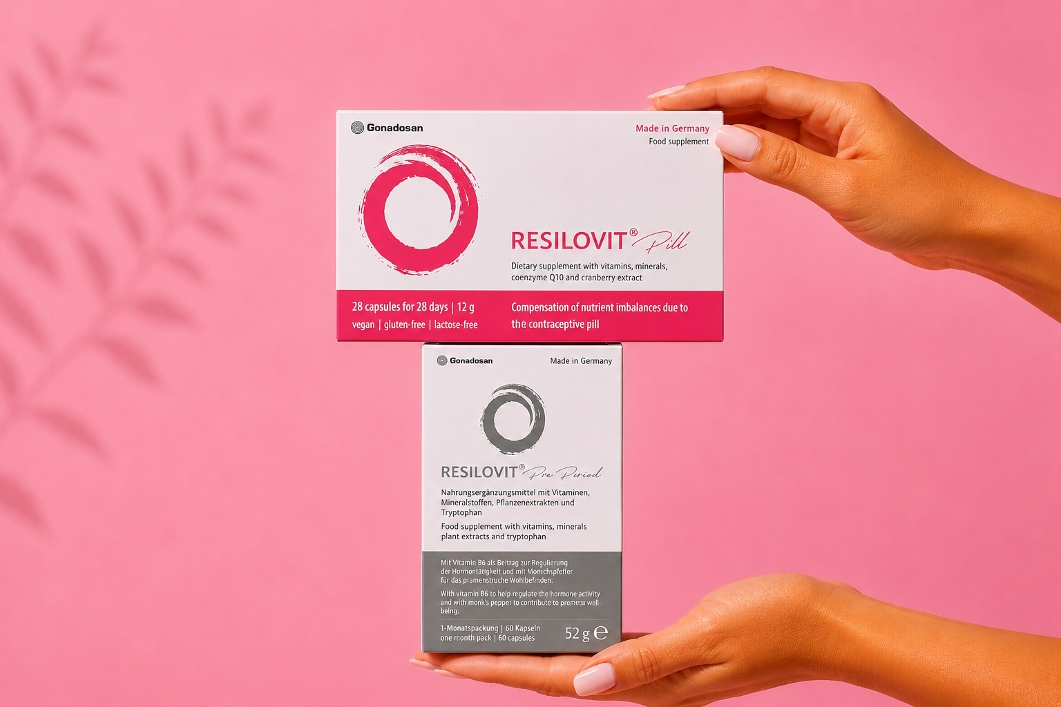 Hands hold a white and pink Resilovit pill box above a gray Resilovit box against a pink backdrop, branding visible.