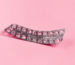 Curved blister pack with mostly empty pill slots on a pink background.