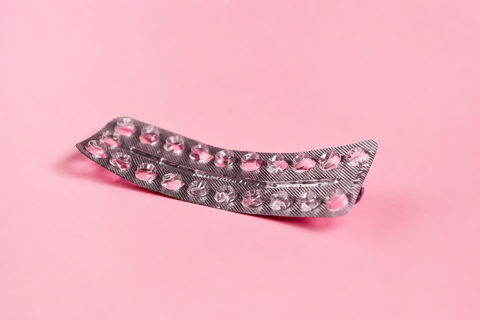 Curved blister pack with mostly empty pill slots on a pink background.